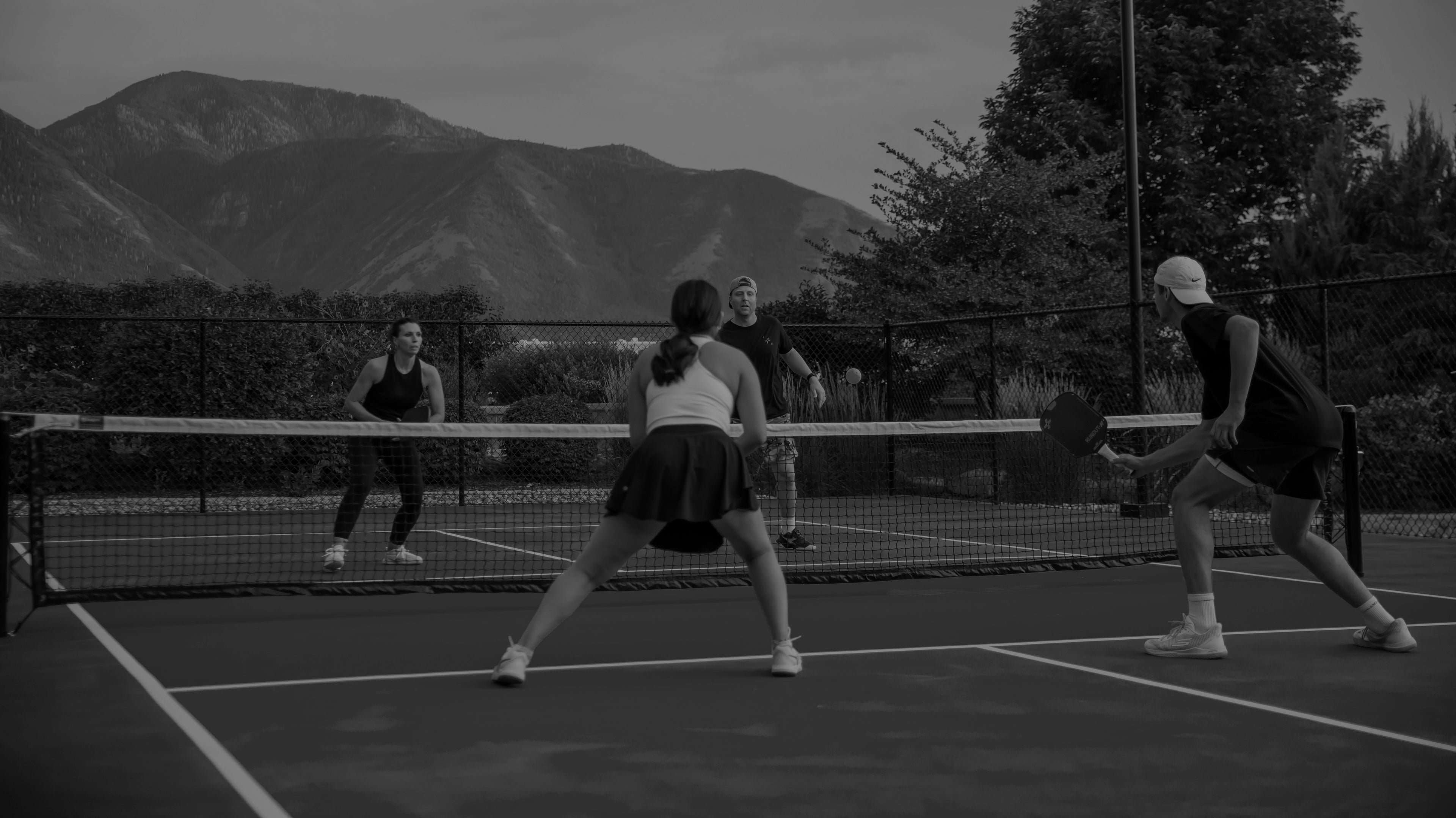 Black and white photo of people playing pickleball with F+B Paddles, on a court with mountains in the background