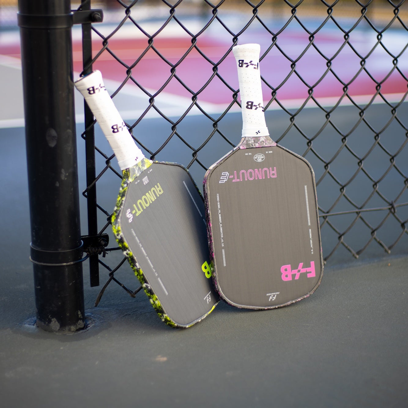 Two pickleball paddles leaning against a chain-link fence on a court.