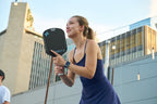 Woman holding the Runout - Standard carbon fiber pickleball paddle outdoors with buildings in the background