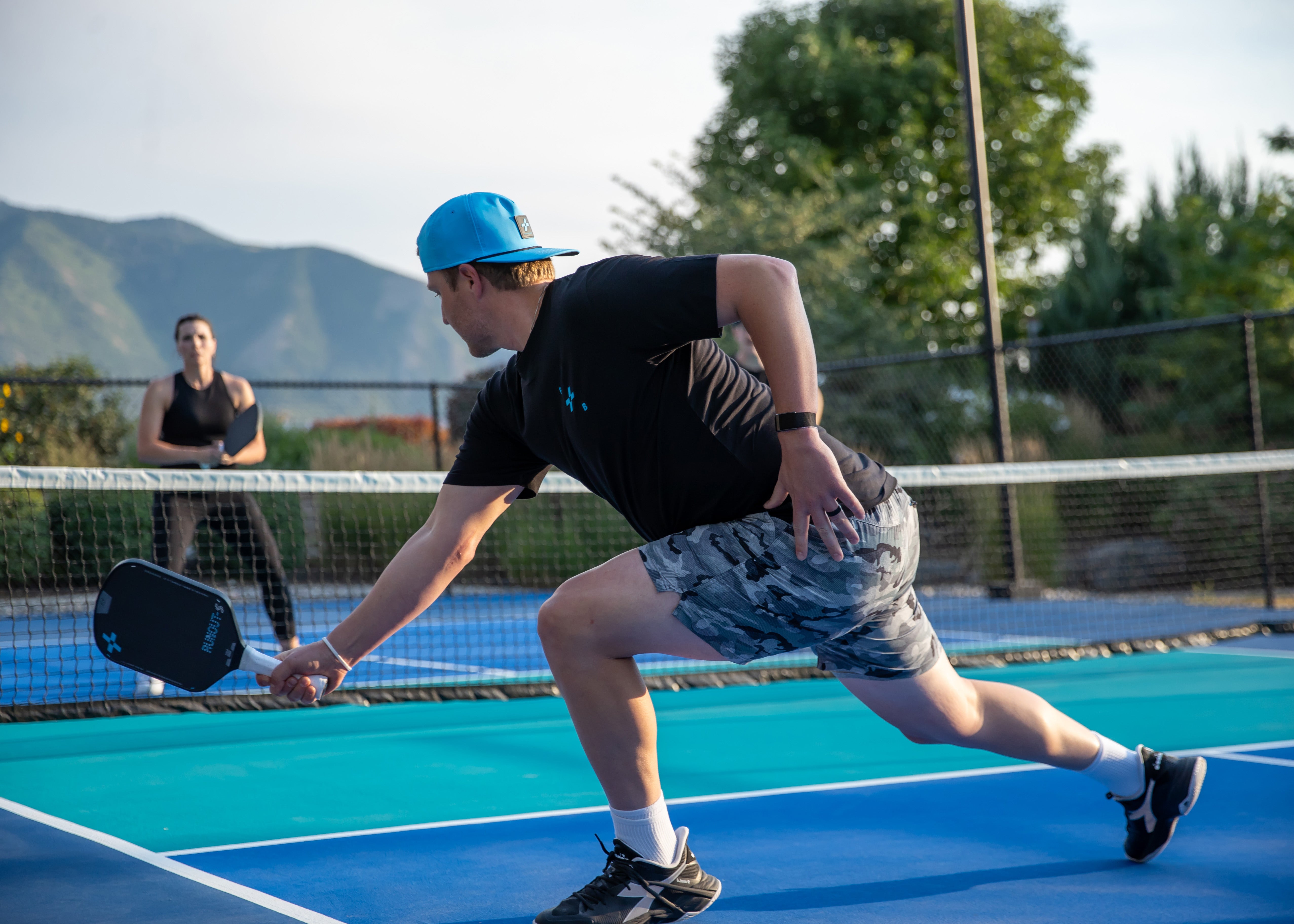 Person playing pickleball on an outdoor court with mountains in the using background using F+B carbon fiber pickleball paddle