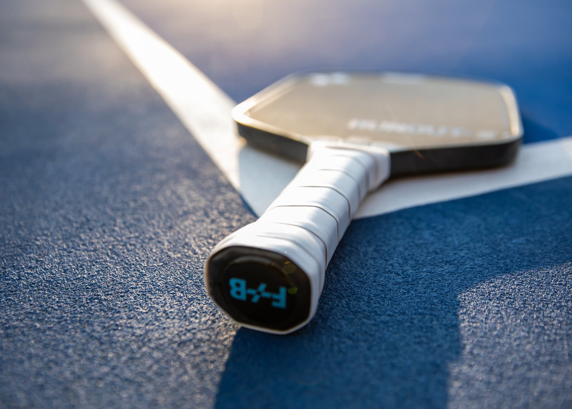 Close-up of a F+B carbon fiber pickleball paddle on a blue surface