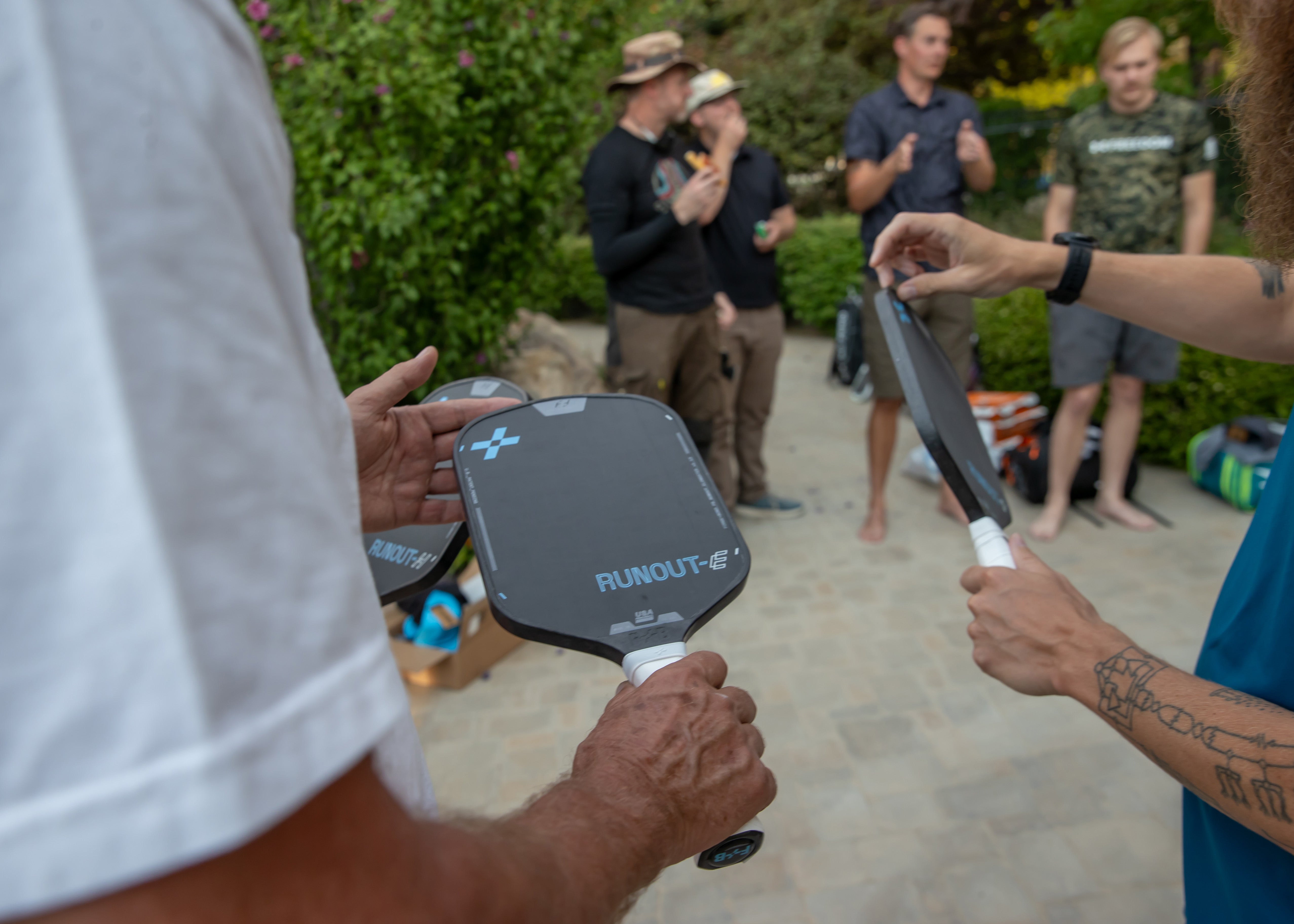 Two people holding F+B pickleball paddles outdoors, surrounded by a group of people.