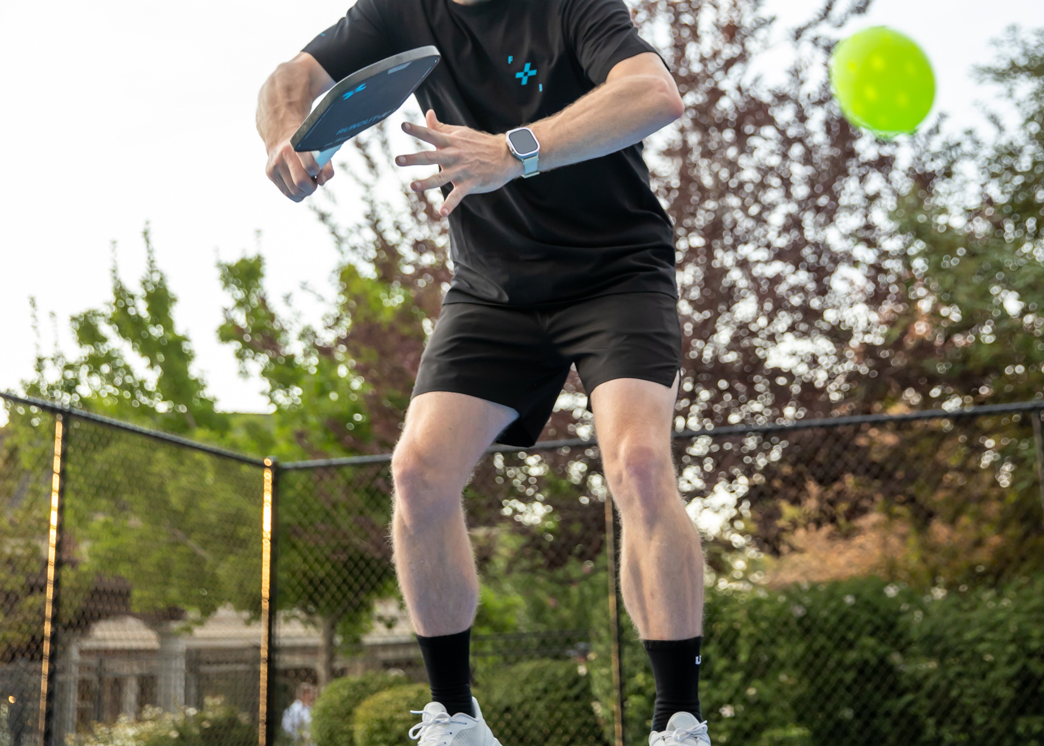 Person playing paddle ball on a court with trees in the background using F+B carbon fiber pickleball paddle